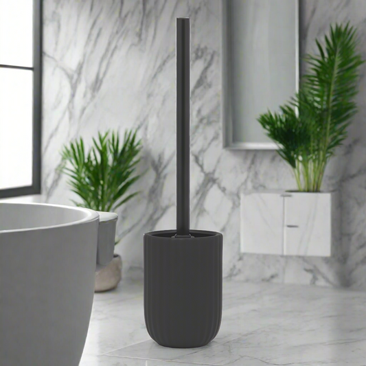 Black stoneware toilet brush holder on bathroom counter against marble wall with green plants